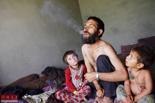 2013年5月21日，在阿富汗拉格曼省，一名44岁的男子在家中吸食鸦片，他的两个孩子在旁边看着他。