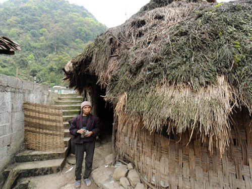 贵州省荔波县瑶山乡巴平村弄哄组，66岁的村民蒙二妹站在自家居住的房屋前，她和儿子兰金华住的茅草房已有几十年历史，是用树枝、竹片拼成的（3月22日摄）
