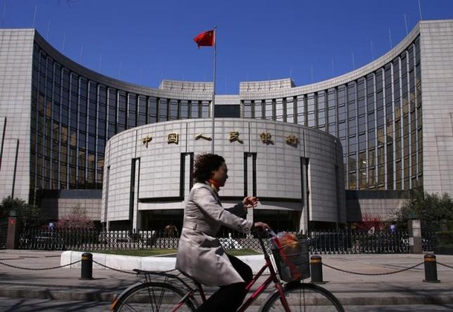 A woman rides past the headquarters of the People's Bank of China in Beijing