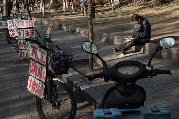  上周，沈阳一名男子在人行道上等候工作机会。失业的工人用挂在电瓶车上的牌子宣传自己的技能。